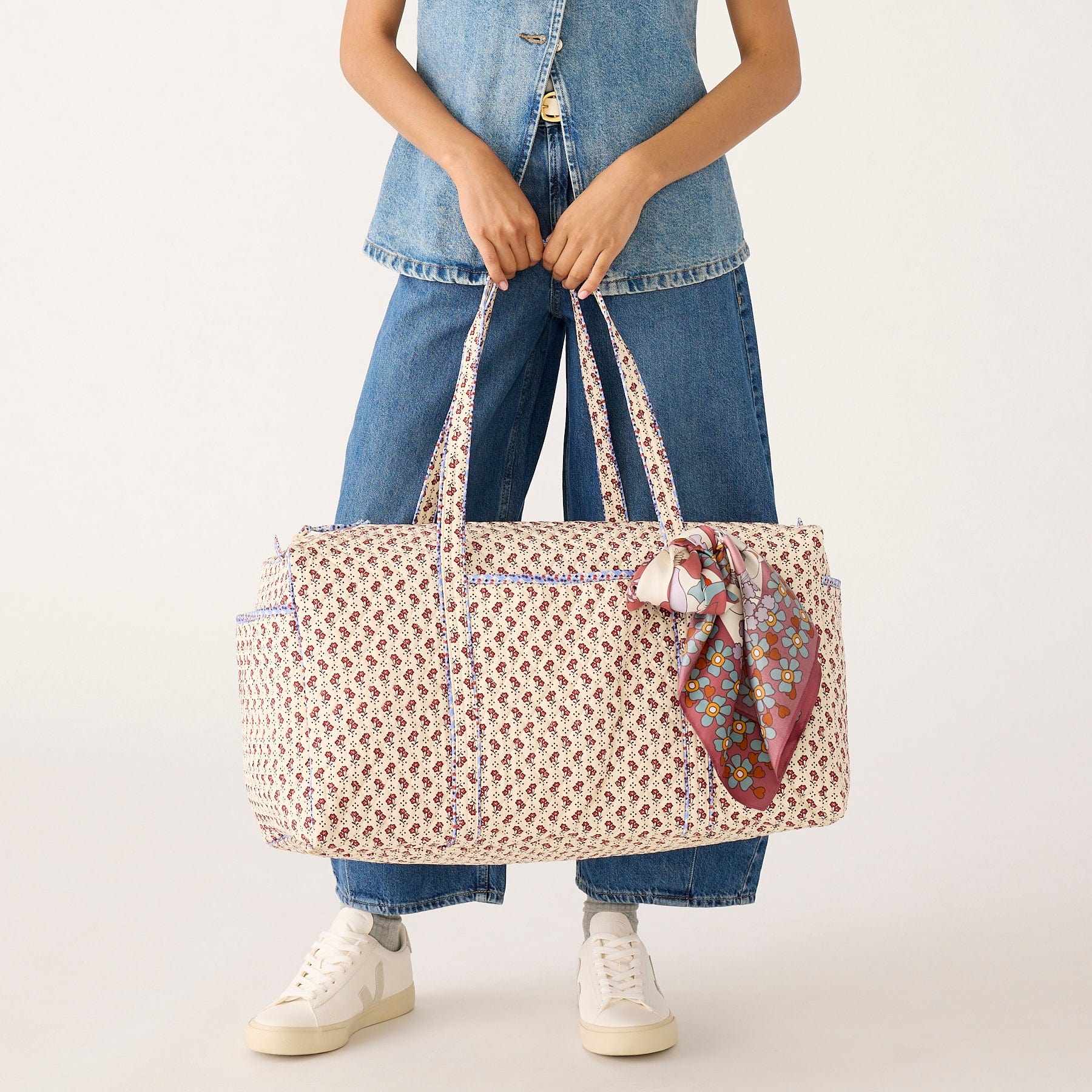 model wearing denim holding large quilted cream colored duffel bag with small red flowers pattern