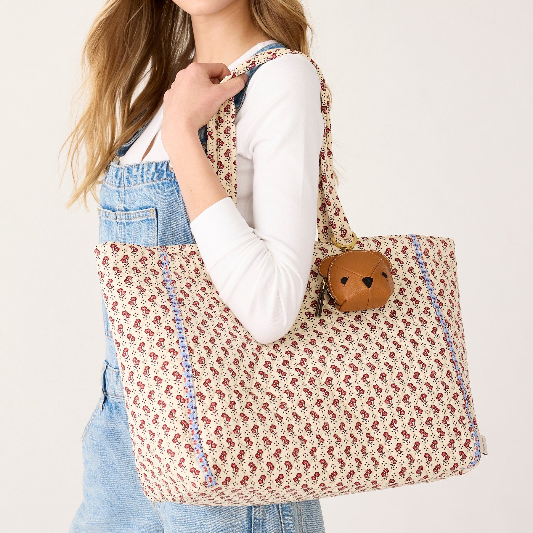 model wearing demin shirt with large beige tote bag over shoulder with small red flowers pattern and bear shaped bag charm